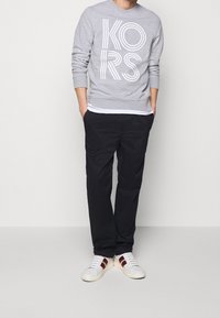 Felpa grigia con logo bianco "KORS", con polsini a costine, abbinata a pantaloni neri e sneakers bianche con dettagli bordeaux.