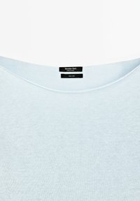 Encolure de chemise en lin bleu clair avec deux étiquettes noires indiquant "Massimo Dutti Made in China" et "100 % lin".