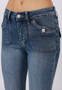Denim jeans with a light blue wash, featuring two front pockets, a coin pocket, and a single button closure at the waistband. Smooth texture.