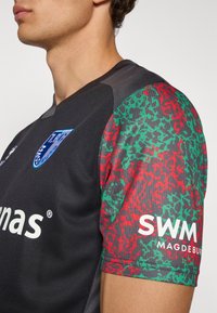 Black sports jersey with textured fabric. Colorful red and green patterned sleeves. Features logos on chest and sleeve. Crew neckline.