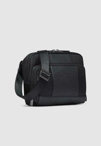 Schwarze Umhängetasche mit einer Mischung aus glatten und strukturierten Materialien, ausgestattet mit zwei Reißverschlussfächern und einem verstellbaren Trageriemen.