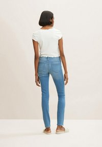Top blanco acanalado con bordes festoneados, combinado con jeans ajustados de algodón azul claro que presentan un diseño clásico de cinco bolsillos y un ligero estiramiento.