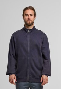 Dunkelblaue Zip-Jacke mit hohem Kragen, lockerer Passform und langen Ärmeln. Hergestellt aus weichem Material mit sichtbaren Stichausführungen.