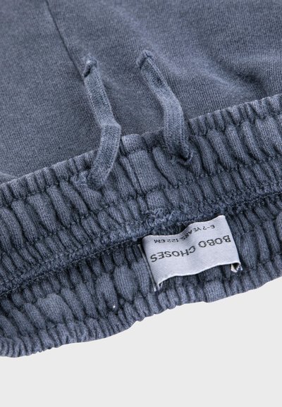 Gros plan sur une ceinture élastique bleue avec cordons de serrage et une étiquette en tissu indiquant la taille et les détails de la marque.