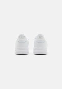 Hvite lær sneakers med tekstur, med rund tå, flat hvit såle og preget "L001" og "LACOSTE" branding på hælen.