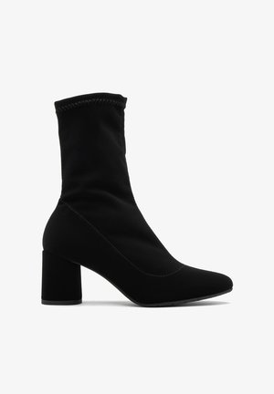 Melnas potītes zābaki, kas izgatavoti no gludas auduma ar norādītu pirkstu un masīvu papēdi. Iespējas pretstatā šuvēm un piegulstoša, elastīga dizaina.