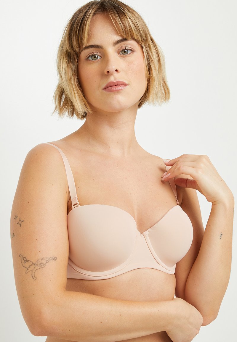Reggiseno color beige con coppe modellate e lisce e spalline regolabili. Presenta una chiusura a gancio e occhiello e un design senza cuciture per un aspetto elegante.