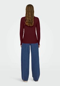 Pull en bordeaux à manches longues avec une taille ajustée, associé à un jean en denim bleu à jambes larges. Texture douce et design minimaliste.