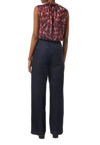 Czerwono-czarny top bez rękawów w wzory, z zebranym dekoltem, w połączeniu z szerokimi, ciemnoniebieskimi dżinsami z widocznym przeszyciem i tylnymi kieszeniami.