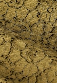 Gros plan sur un tissu jaune moutarde avec un motif de dentelle florale et un fond tissé texturé.
