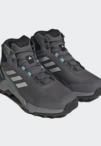 Scarpe da trekking grigie con tomaia in mesh e sintetico, caratterizzate da tre strisce bianche e accenti in teal, suole testurizzate per una maggiore trazione.