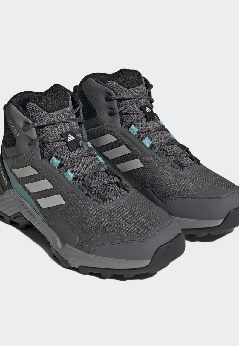 Szare buty trekkingowe z siateczkowymi i syntetycznymi wstawkami, z trzema białymi paskami i akcentami w odcieniu teal, teksturowane podeszwy zapewniające dobrą przyczepność.