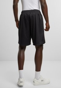Pantaloni corti sportivi neri con vita elastica, design fino al ginocchio e tessuto traspirante. Sneakers bianche e calzini completano l'outfit.