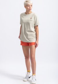 Lichtbeige katoenen T-shirt met korte mouwen, voorzien van een kleine grafische print. Gepaard met oranje shorts en witte hoge sneakers.