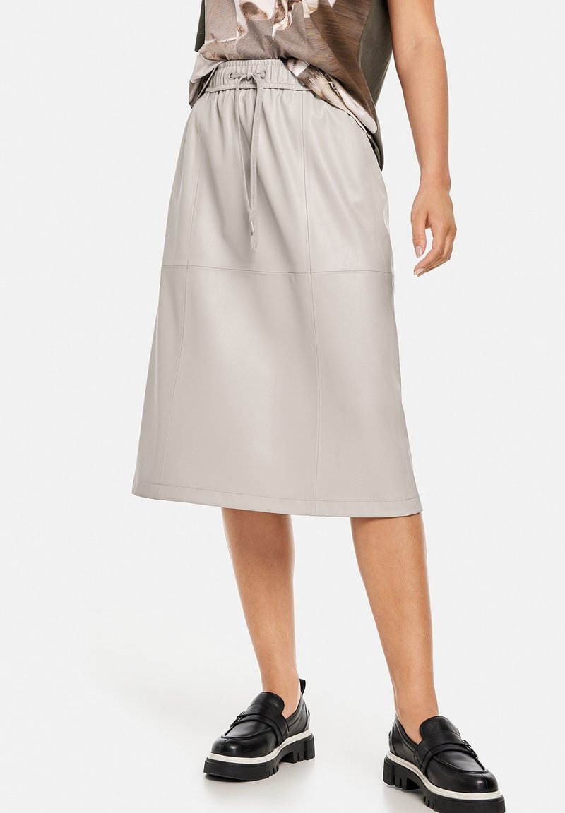 Jupe midi en cuir gris clair avec une ceinture élastique et un cordon de serrage. Dotée de coutures verticales et d'une texture lisse. Associée à des chaussures noires.