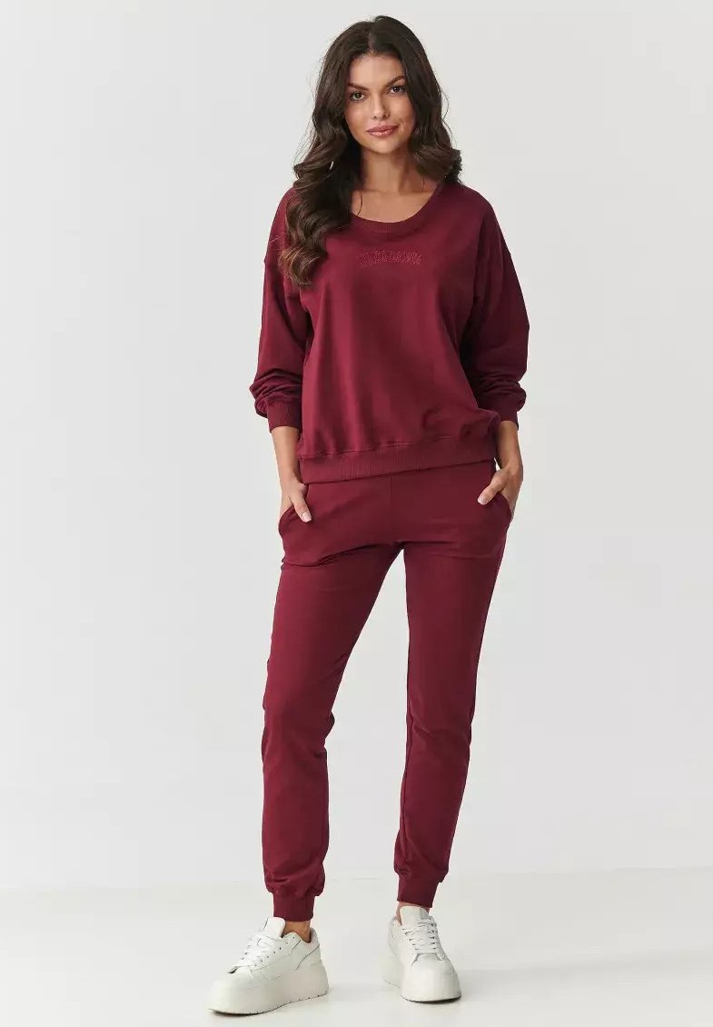 Burgundowy zestaw bluzy i spodni dresowych wykonany z miękkiej tkaniny; charakteryzuje się luźnym krojem, ściągaczami przy rękawach oraz bocznymi kieszeniami dla wygody.