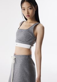 Top corto grigio con un design aderente, tessuto texturizzato e una banda elastica bianca all'orlo. Presenta un dettaglio con zip laterale.