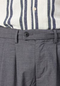 Gray tailored trousers with a flat front, featuring a black button closure and side pockets. Material appears textured and lightweight.
