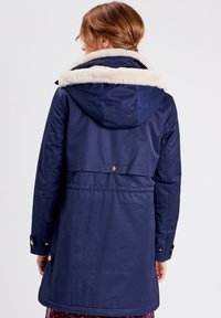 Granatowa kurtka z sztucznym futrem na kołnierzu, o długości średniej, z zapięciami na zatrzaski i ściągaczem w talii, charakteryzująca się gładką fakturą.