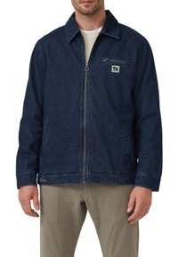 Dunkelblaue Jeansjacke mit einem Reißverschluss vorne, Brusttasche und Seitentaschen. Hat einen Kragen und ein minimales Branding-Detail auf der Brust.