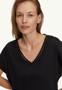 Zwart V-hals shirt met korte mouwen, voorzien van een subtiele doorzichtige rand langs de halslijn. Smooth textuur, casual pasvorm.