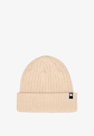 Gorro de punto en beige con textura acanalada, que presenta un dobladillo enrollado y un pequeño parche de logo negro en el costado.