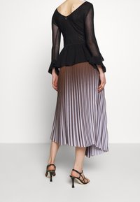 Czarna, przezroczysta bluzka z długim rękawem o prążkowanej fakturze, w zestawieniu z plisowaną spódnicą przechodzącą z brązowego w lawendowy. Czarne sandały na wysokim obcasie z paskami.