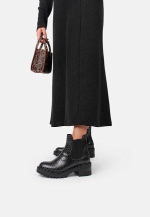 Bottes Chelsea en cuir à motif serpent noir avec une semelle épaisse et des panneaux élastiques sur les côtés, associées à une longue jupe noire et un sac à main à imprimé léopard.