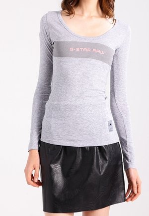 Chemise grise à manches longues avec un décolleté en creux et un logo horizontal G-Star RAW en rose. Associée à une mini-jupe en cuir noire.