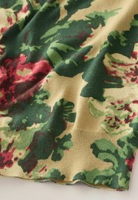 Gebreide trui met een bloemenpatroon in tinten groen en rood op een beige achtergrond, met een gestructureerde afwerking en geribde zoom.