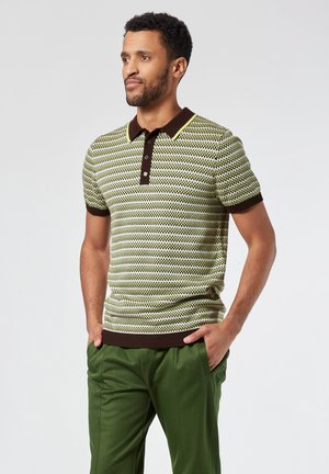 Polo de rayas horizontales verdes y crema, con cuello y puños en contraste marrón, hecho de tejido de punto, combinado con pantalones verdes.