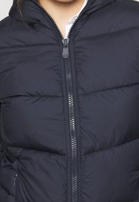 Doudoune navy avec fermeture éclair et capuche. Présente une texture matelassée et des détails de couture visibles le long des coutures.