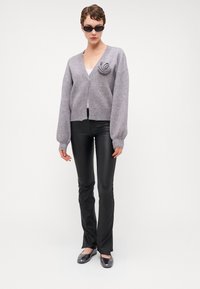 Sivý pletený kardigán so špirálnym akcentom, skombinovaný s čiernymi koženými nohavicami a sivými balerínami. Model má na sebe elegantné čierne slnečné okuliare.