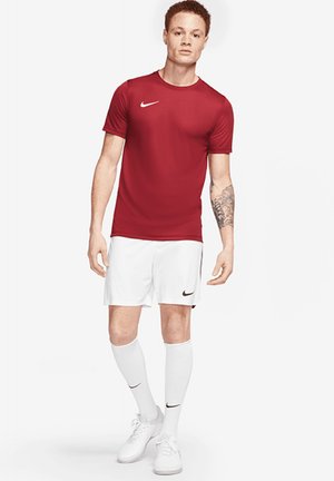 Maglietta sportiva rossa, pantaloni corti bianchi, calzini bianchi e sneakers bianche. Presenta il logo Nike sulla maglietta e sui pantaloni corti; design aderente, texture liscia.