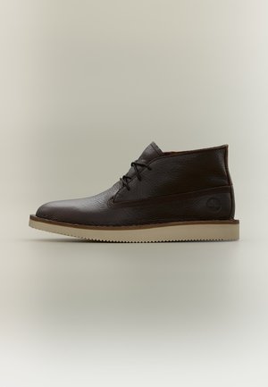 Mørkebrun læderankelstøvle med sorte snørebånd og beige sål, vist i sideprofil mod en enkel neutral baggrund.