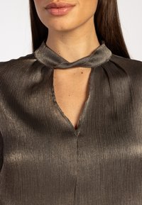 Blouse gris métallisé foncé avec une finition texturée, un col torsadé et un détail d'encolure en forme de goutte d'eau. Tissu lisse avec des lignes verticales.