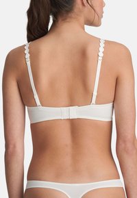 Bralette blanca con detalles decorativos de tirantes con forma de ondas, cierre de gancho y ojal, y un diseño liso y sin costuras. Estilo minimalista.