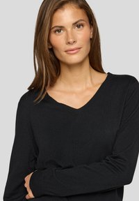 Schwarzer V-Ausschnitt-Pullover mit langen Ärmeln. Weiche Textur, figurbetontes Design und gerippte Bündchen. Minimale Details, ideal zum Schichten geeignet.