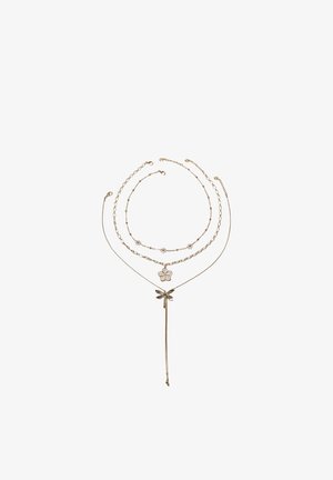 Drie delicate gouden kettingen met verschillende kettinestijlen, met bloem- en libellebedels op een witte achtergrond.