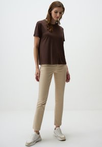 Bruine T-shirt met korte mouwen gecombineerd met beige slim-fit broek en witte sneakers. De T-shirt heeft een relaxte pasvorm en een soepele textuur.