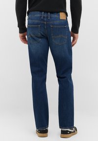 Jeans in denim blu scuro con design a gamba dritta, cuciture arancioni in contrasto e una patch in pelle sulla cintura posteriore. Due tasche posteriori visibili.
