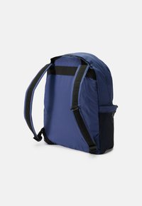 Mochila azul marinho com alças acolchoadas, tecido de nylon suave e um bolso em malha lateral. Design simples e funcional, ideal para uso diário.