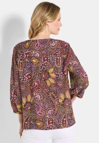 Langärmlige Bluse mit floralem Paisleymuster in verschiedenen Lila-, Rosa- und Grüntönen auf dunklem Hintergrund; entspannte Passform mit gerafften Ärmeln.