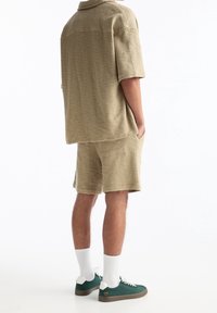 Beige kurzärmeliges Shirt mit Struktur und passende Shorts, kombiniert mit grünen Turnschuhen und weißen Socken. Auffälliger gewebter Stoff und entspannte Passform.