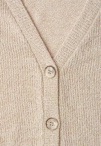 Lähikuva beige neulottu neuletakki, jossa on kaksi suurta marmoroitua nappia ja V-kauluksen yksityiskohta.