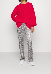 Rød oversized strikket sweater med ribbet tekstur, parret med grå slangeskinsmønstrede slim-fit bukser og hvide sneakers.