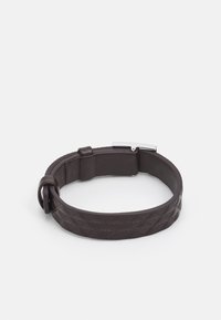 Pulsera de cuero en marrón oscuro con un patrón texturizado de formas de diamante. Presenta un cierre metálico, un diseño elegante y un ajuste ajustable.