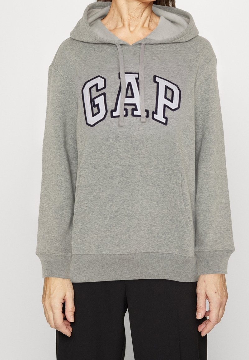 Sudadera gris con un bolsillo canguro, presenta un logo de "GAP" en navy en el pecho. Diseñada con capucha ajustable y puños acanalados.