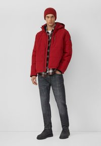 Czerwona ocieplana kurtka z kapturem, pod spodem koszula w kratę, ciemne dżinsy i czarne buty. Elementy charakterystyczne to kieszeń na zamek oraz dzianinowa czapka z fakturą.