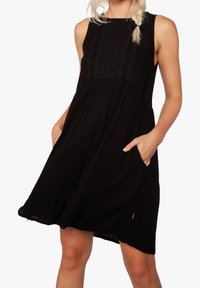 Vestido negro sin mangas hecho de tela ligera, con un cuerpo texturizado que presenta costuras decorativas y bolsillos laterales. Silueta fluida.